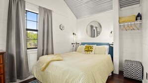 Un dormitorio con cama, una ventana con cortinas, una mesita de noche, un espejo y un armario.