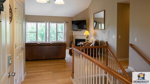 A spacious living room with hardwood floors, a fireplace, a large window, and a staircase. - 4BR Duplex w/ Hot Tub & Fire Pit | Pet Friendly | Group Stay | DV 166 (Branson)
