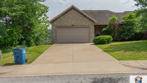 A single-story house with a garage, a driveway, and a blue trash bin. - 4BR Duplex w/ Hot Tub & Fire Pit | Pet Friendly | Group Stay | DV 166 (Branson)