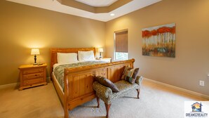 A bedroom with a wooden bed, a nightstand, a bench, and a painting on the wall. - 4BR Duplex w/ Hot Tub & Fire Pit | Pet Friendly | Group Stay | DV 166 (Branson)