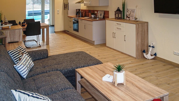 A modern living room with a grey sectional sofa, a wooden coffee table, and a kitchen area with white cabinets and a wooden countertop. - 2 bedroom nice home in Gützkow (Gützkow)