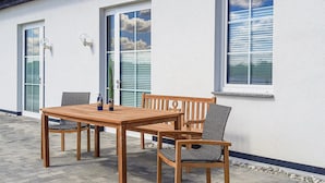 An outdoor patio with a wooden table and chairs, a potted plant, and a wall-mounted light fixture. - 2 bedroom nice home in Gützkow (Gützkow)