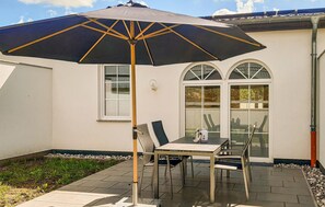 An outdoor patio with a table and chairs, a large umbrella, and a white building with arched windows.