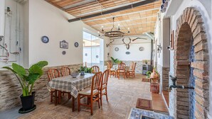 Un comedor con una mesa y sillas de madera, rodeado de plantas en macetas y platos decorativos en las paredes.