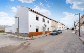 Une rue tranquille, bordée de bâtiments blancs, de voitures garées et sous un ciel dégagé.