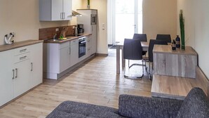 Una cocina compacta con electrodomésticos modernos, un comedor con mesa y sillas de madera, y vistas al exterior a través de un ventanal grande.
