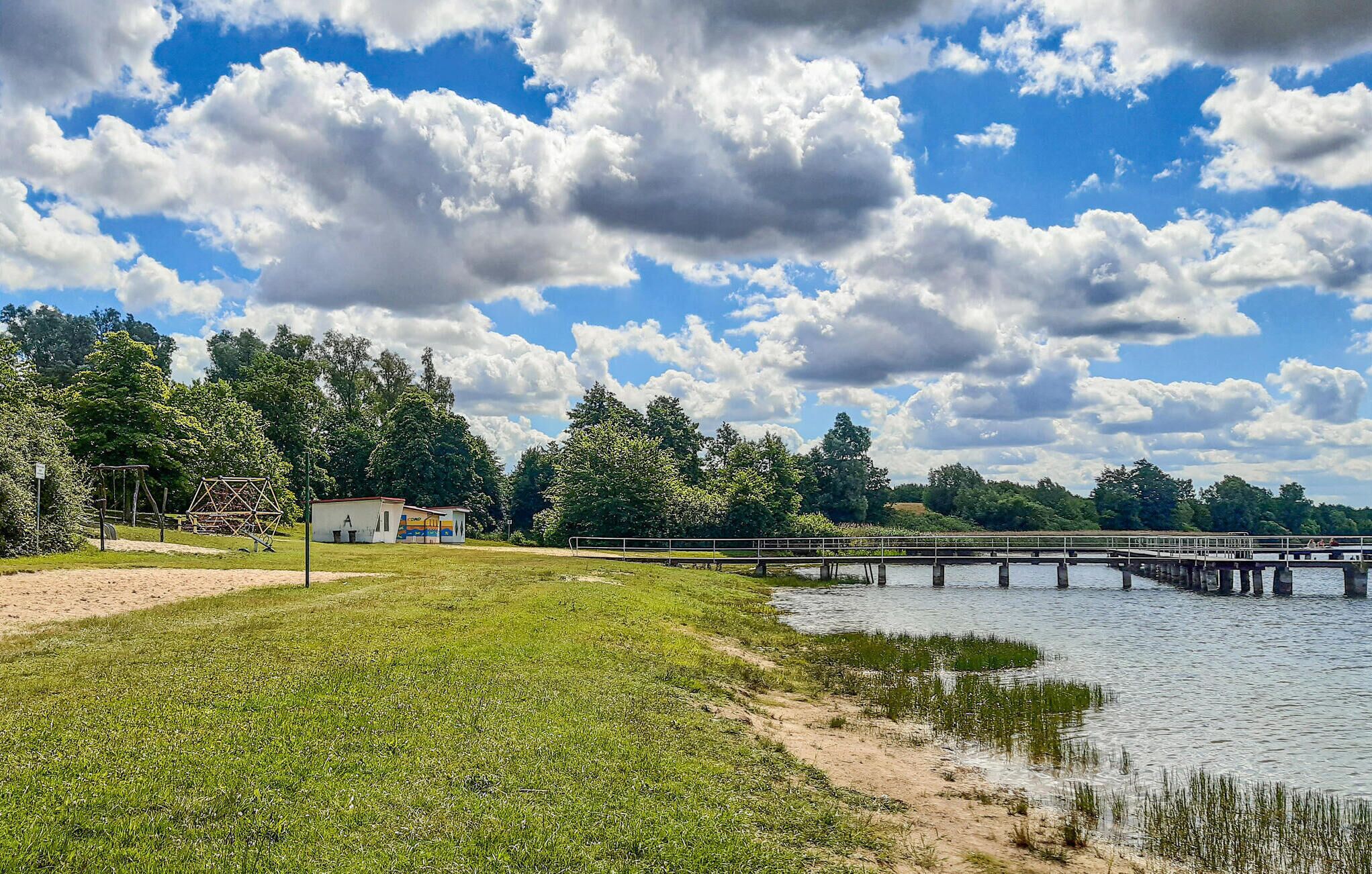 A park with a grassy area, a small building, and a bridge over a body of water.
