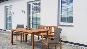 Un patio exterior con una mesa y sillas de madera, una planta en maceta y un aplique de pared.