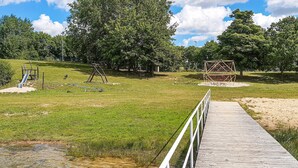 Un muelle de madera que conduce a un parque infantil con columpios y un tobogán.