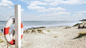 A lifeguard tower with a red and white lifebuoy on a sandy beach with a calm sea and clear sky. - 3 bedroom amazing home in Glesborg (Glesborg)