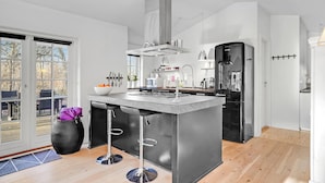 A modern kitchen with a central island, stainless steel appliances, and a view through the glass door. - 3 bedroom amazing home in Glesborg (Glesborg)