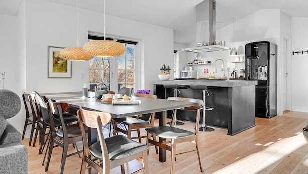 A modern kitchen with a central island, a dining area with wooden chairs, and a large window providing natural light. - 3 bedroom amazing home in Glesborg (Glesborg)