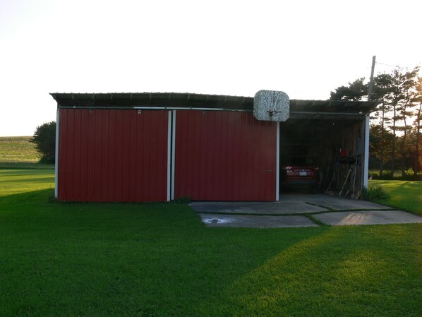 A red metal shed with a garage door, a small attached structure with a window, and a paved entrance.