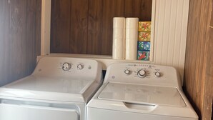 A laundry room with two front-loading washers and dryers, wooden walls, and a shelf with towels and a colorful box. - Lever Hill Lodge (Andover)