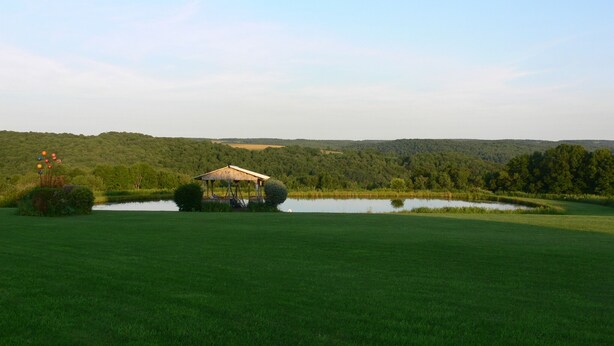 A golf course with a pavilion on a small pond surrounded by lush greenery and hills in the background. - Lever Hill Lodge (Andover)
