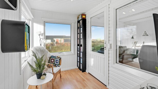 A room with a large window, a bookshelf, a white chair, a small table with a plant, and a view of the outside. - Amazing home in Vinderup with WiFi (Vinderup)