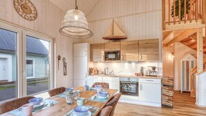 Een moderne keuken met houten keukenkastjes, een magnetron en een fornuis. Er is een eethoek met een houten tafel en stoelen, en een hanglamp.