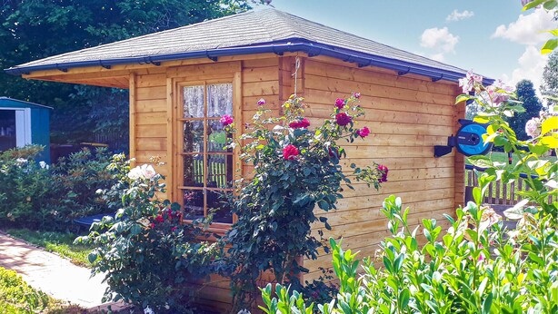 A wooden cabin with a sloped roof, a window, and a garden with various plants and flowers. - 2 bedroom stunning home in Brünlos (Brünlos)