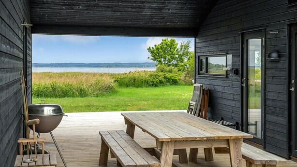 A wooden deck with a table and benches, a grill, and a view of a lake and greenery.