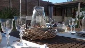 A table set outdoors with clear glassware, a metal pitcher, and a woven basket. - Les Persiennes (Saintes)