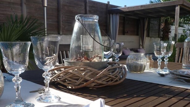 A table set outdoors with clear glassware, a metal pitcher, and a woven basket. - Les Persiennes (Saintes)