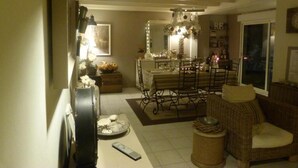 A cozy living room with a dining area, featuring a chandelier, wicker furniture, and a television. - Les Persiennes (Saintes)