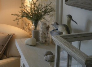 A room with a sofa, a glass vase with dried flowers, a bird figurine, and a small bird figurine on a table. - Les Persiennes (Saintes)