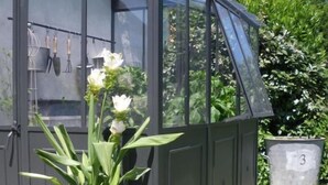A greenhouse with a glass roof, a potted plant in the foreground, and a metal container labeled '3' in the background. - Les Persiennes (Saintes)