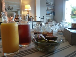 A dining table with two glass bottles, a bowl of fruit, and various glass containers. - Les Persiennes (Saintes)