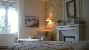 A bedroom with a bed, a chair, a fireplace, a painting, and a window. - Les Persiennes (Saintes)