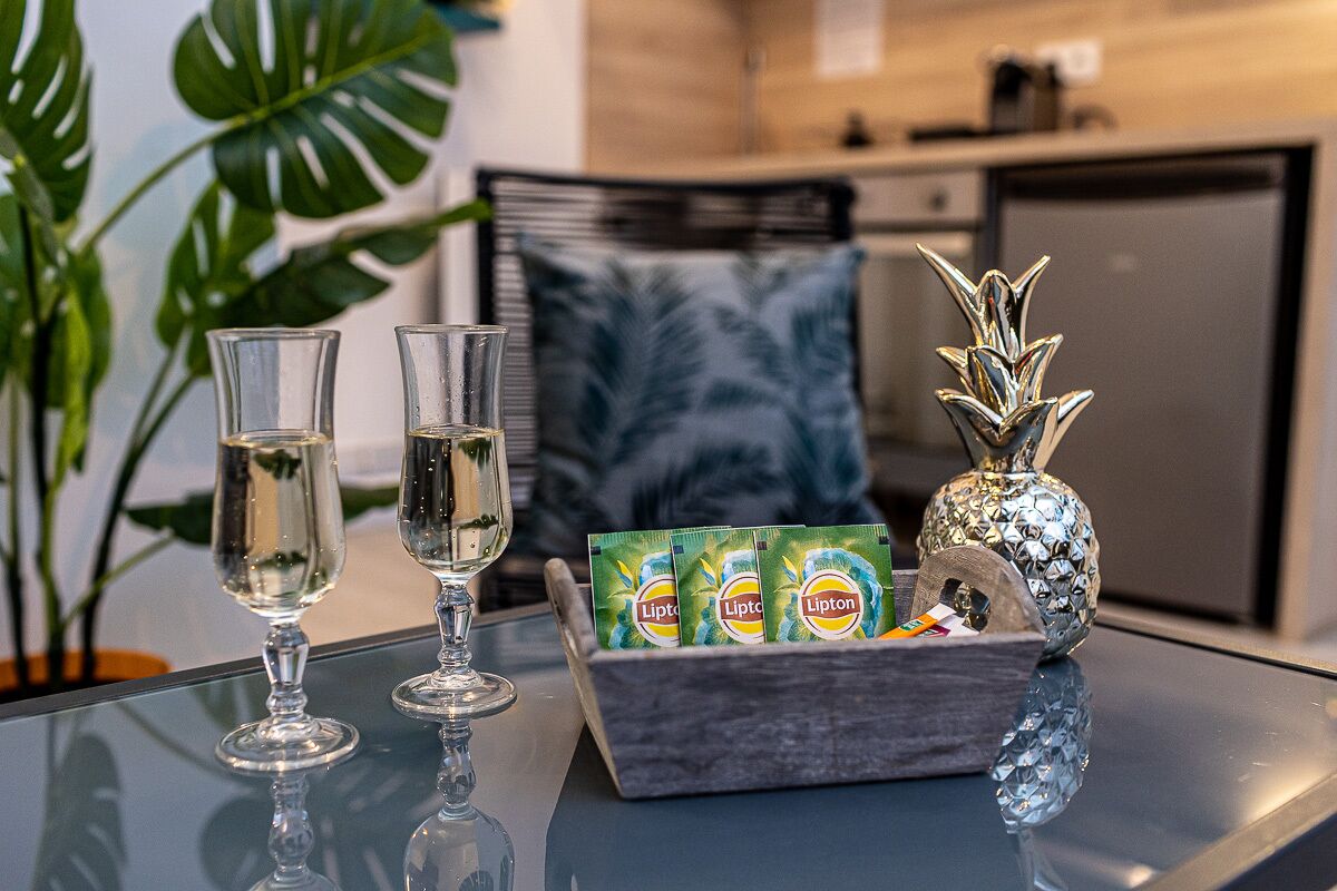 A glass table with two glasses of a clear liquid, a decorative pineapple-shaped vase, and a box of Lipton tea bags.