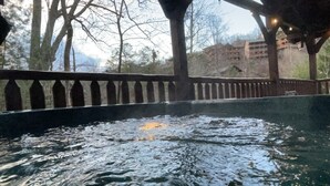 Un espace avec un bain à remous, une terrasse en bois et une vue sur les arbres et les bâtiments en arrière-plan.