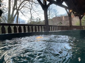 Ein Whirlpoolbereich mit einer Holzterrasse und Blick auf Bäume und Gebäude im Hintergrund.
