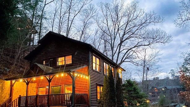 Une cabane en rondins à deux étages, dotée d’un porche et entourée d’arbres.