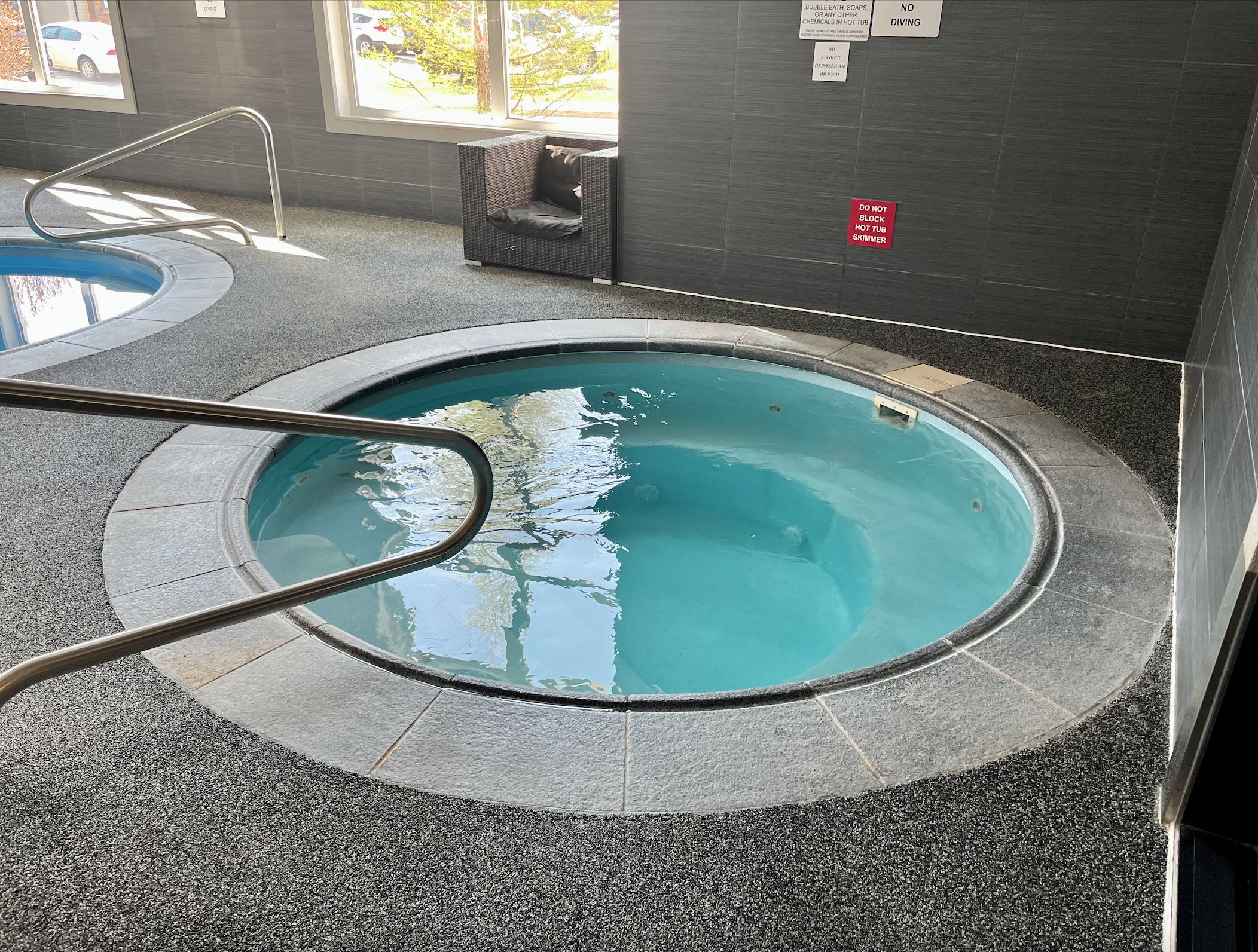 A small indoor pool with a metal ladder, tiled walls, and a window with a view of parked cars.