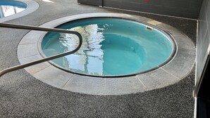 En lille swimmingpool indendørs med en metalstige, flisebeklædte vægge og et vindue med udsigt til parkerede biler.