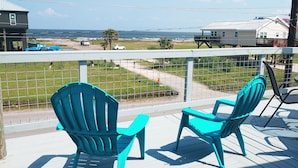 A deck with turquoise chairs and a table, overlooking a beach with houses and a road. - Rica Rico - Beach View Getaway (Grand Isle)