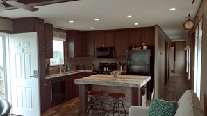A modern kitchen with dark wood cabinets, a central island with stools, a black refrigerator, and a microwave above the island. - Rica Rico - Beach View Getaway (Grand Isle)
