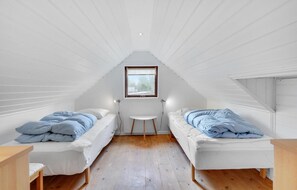Um quarto de sótão pequeno com duas camas de solteiro, uma mesinha e uma janela.
