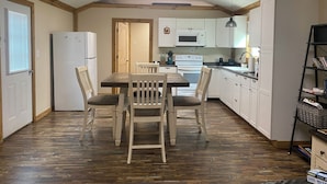 Een compacte keuken met houten vloeren, een eettafel met stoelen, een koelkast, een magnetron, een oven en een spoelbak.
