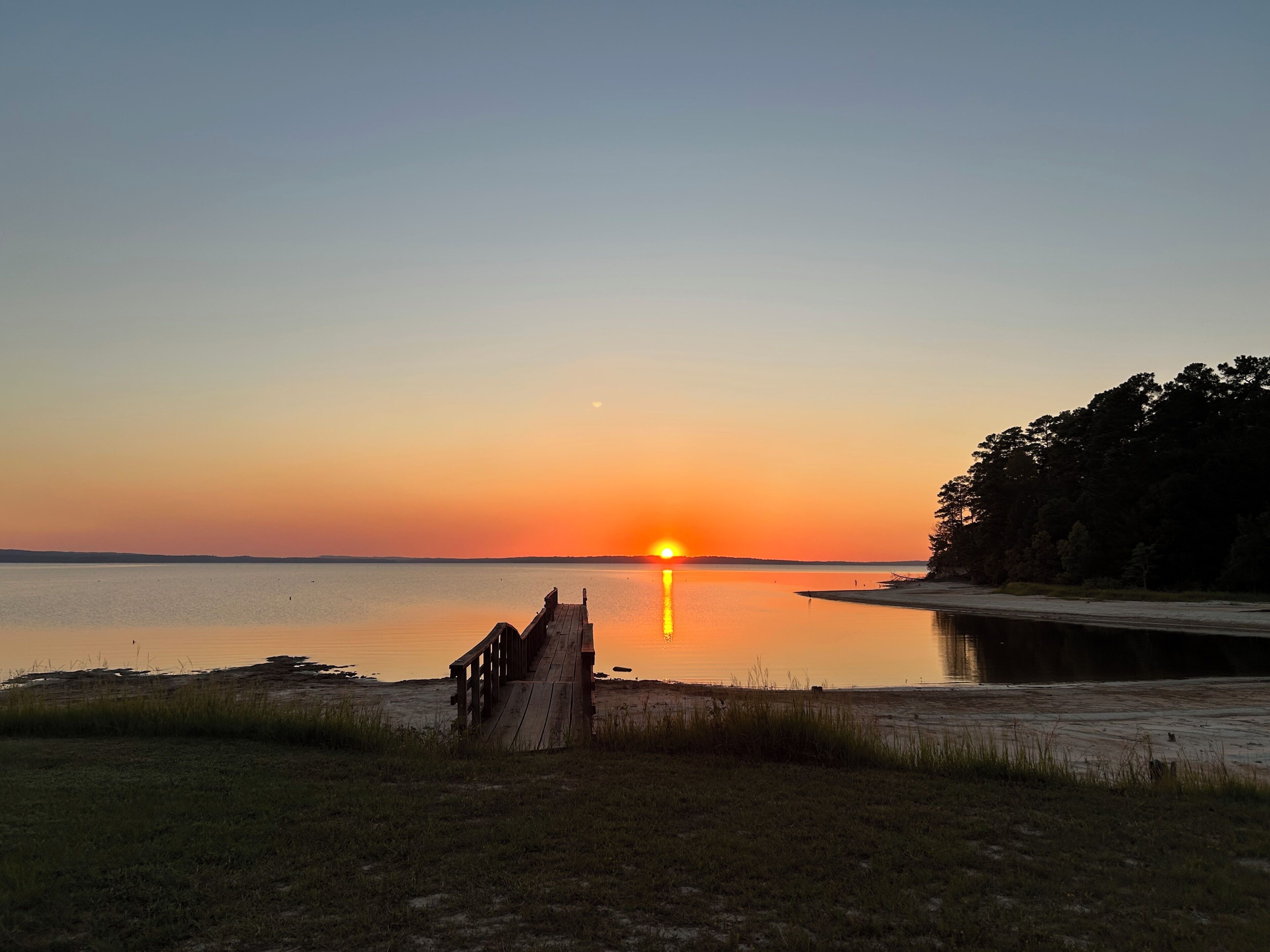 Een zonsondergang boven een rustig wateroppervlak met een houten steiger die in het water reikt.