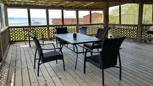 Een overdekt terras buiten, met een tafel en stoelen, met uitzicht op een wateroppervlak.