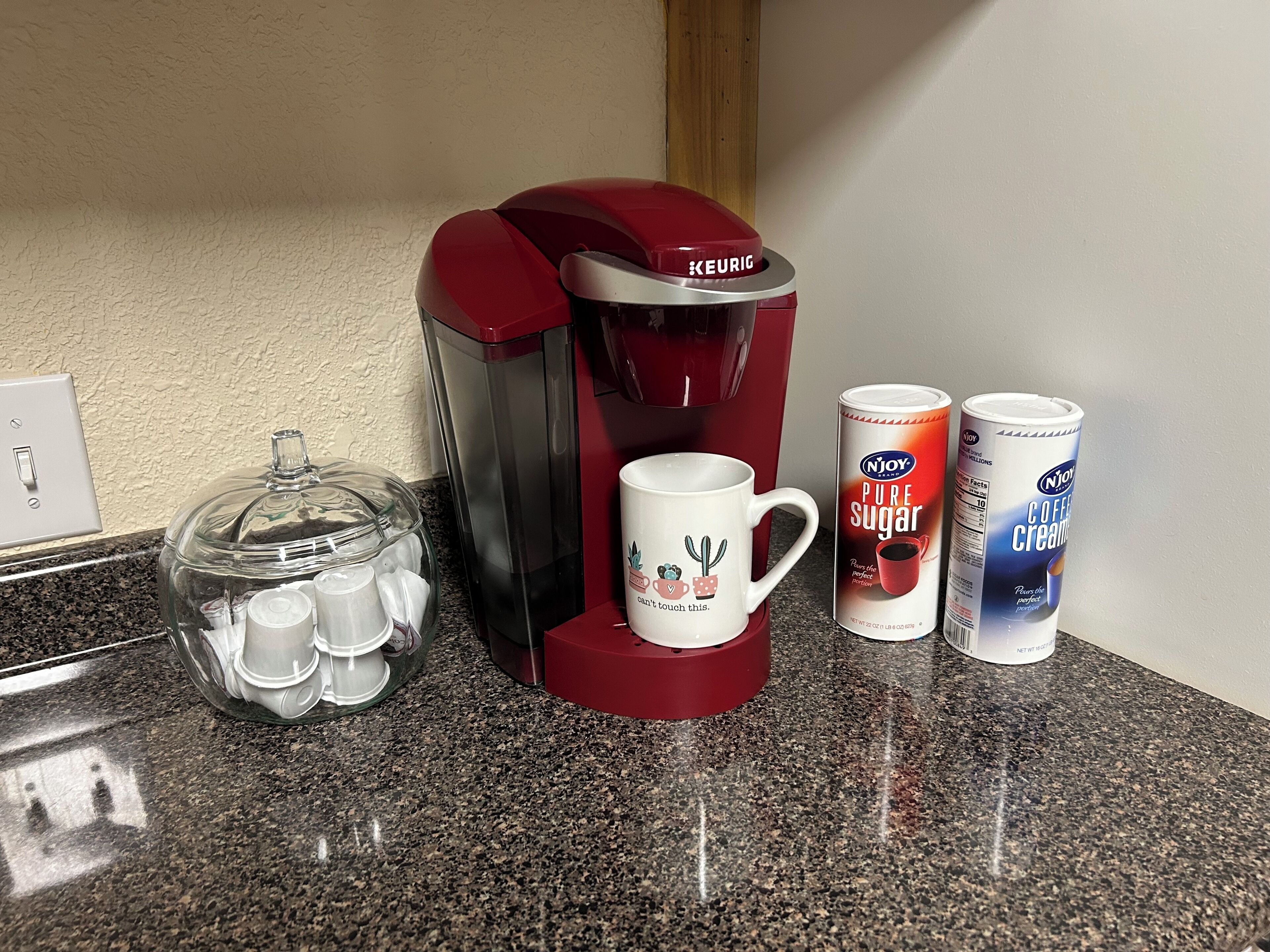 Una cafetera, una taza y dos latas de leche para café sobre una encimera de cocina.