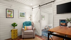 Una habitación con puerta corrediza estilo granero, un sofá con manta, una mesita auxiliar con una planta, un cuadro enmarcado y un televisor en la pared.
