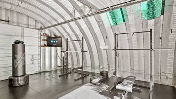 Une salle de sport équipée de matériel de musculation, d’un sac de frappe et d’un écran numérique.