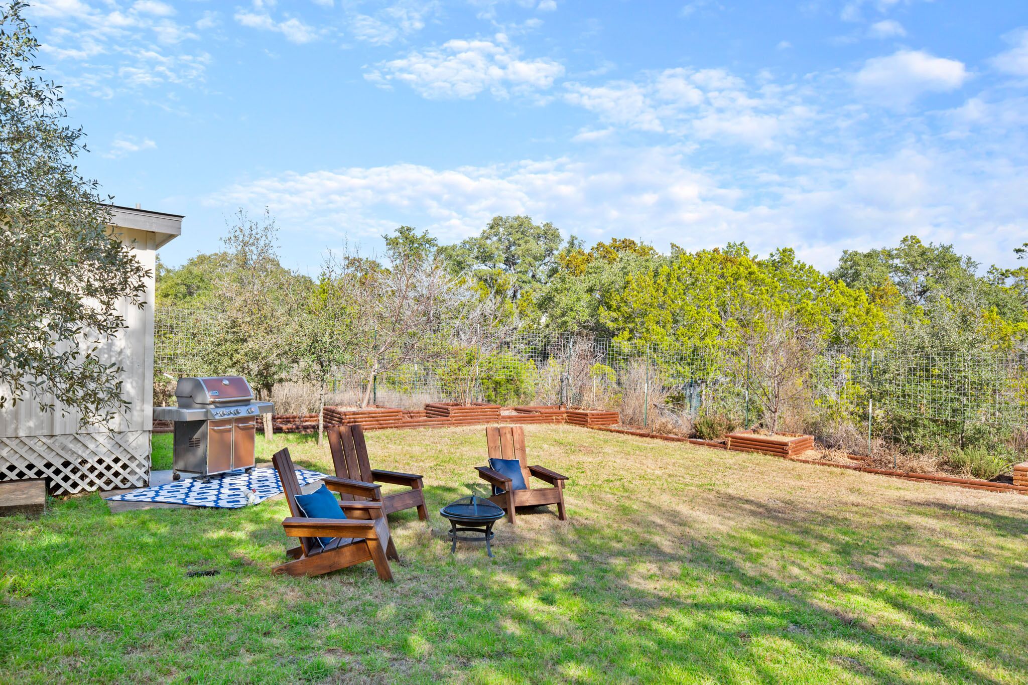 Un jardin avec un barbecue, des chaises en bois et une clôture en treillis.