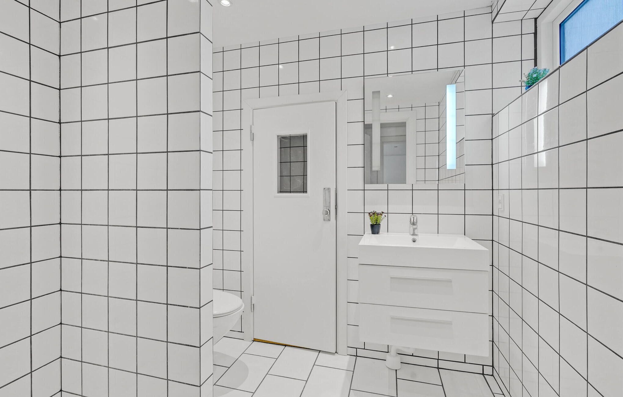 Une salle de bain moderne avec des carreaux blancs, des toilettes, un lavabo et un miroir.