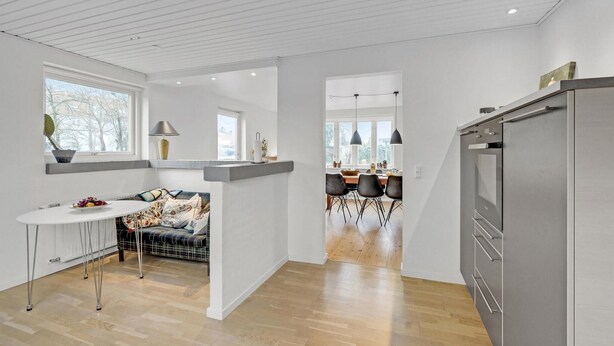 Una cocina moderna con un refrigerador de acero inoxidable, un comedor con una mesa y sillas de madera, y una zona de estar con un sofá y una mesita.