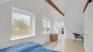 Una habitación amplia con ventanas grandes, una cama, una silla y una cesta de mimbre.