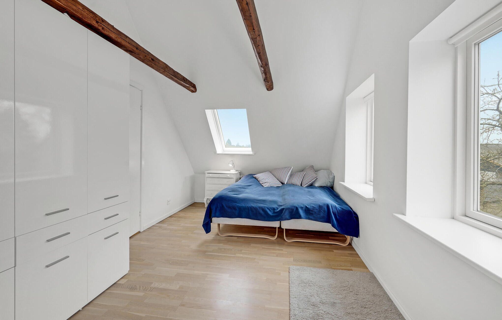 Une chambre avec un plafond en pente, un puits de lumière, un lit avec une literie bleue, une table de chevet et une armoire.
